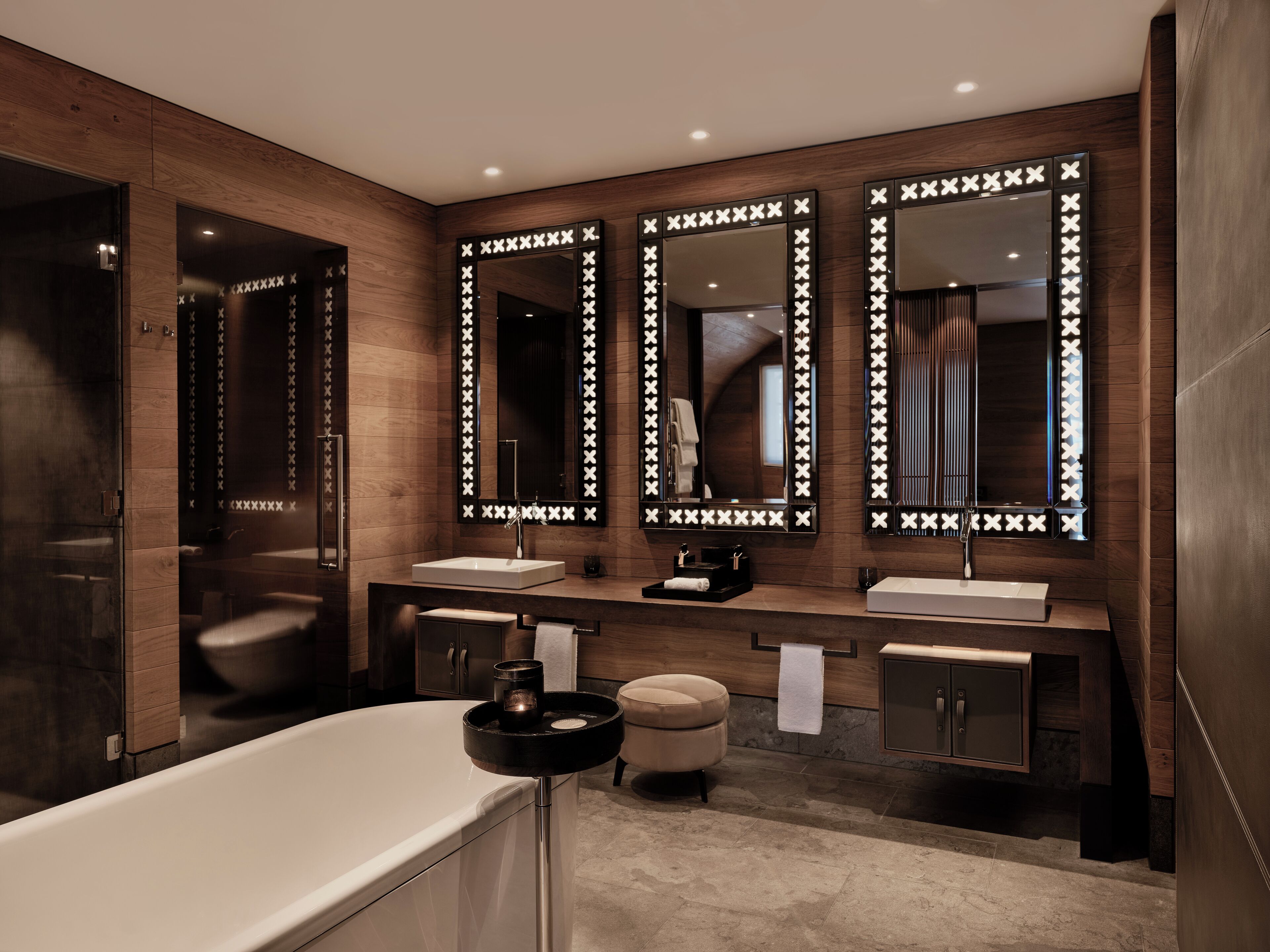 A modern bathroom with a large bathtub, two sinks, and three mirrors with illuminated frames.