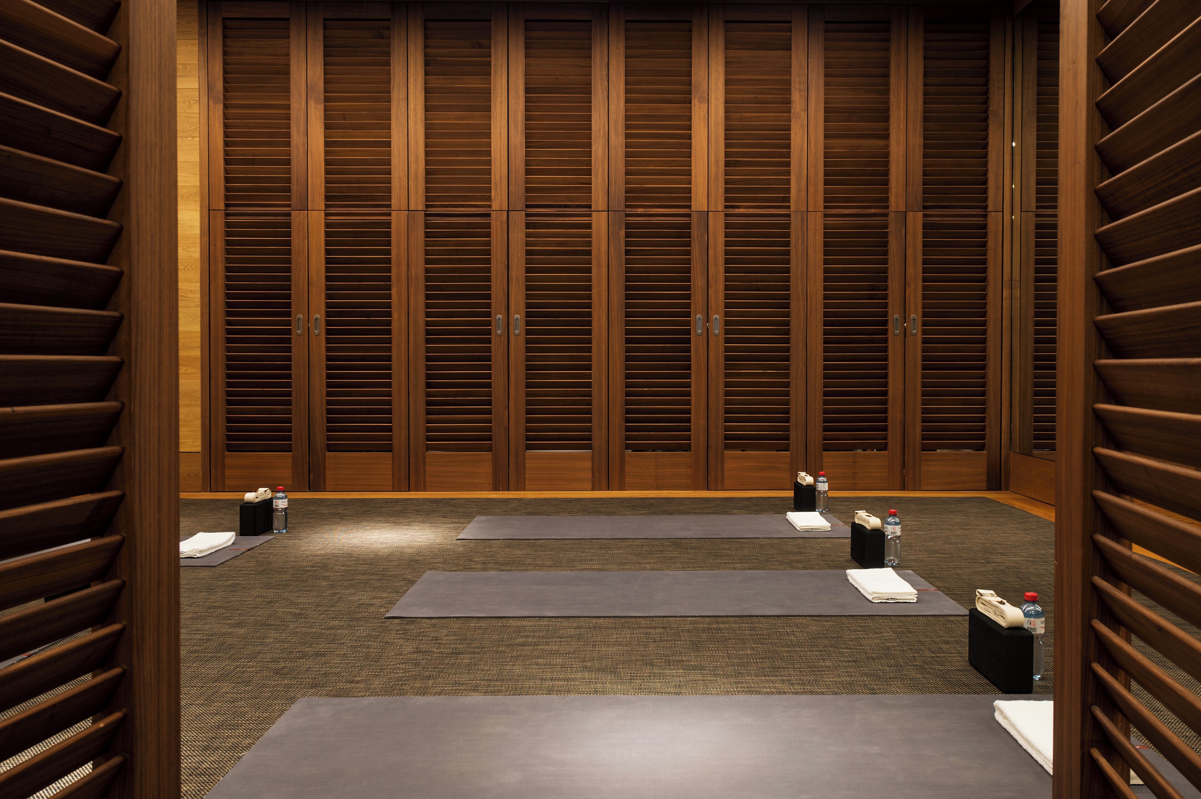 A room with wooden sliding doors, yoga mats, and water bottles on the floor.
