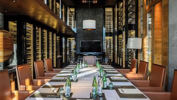 A long dining table set for a formal event, surrounded by leather chairs, with wine bottles and menus.