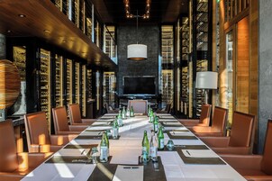 A long dining table set for a formal event, surrounded by leather chairs, with wine bottles and menus.
