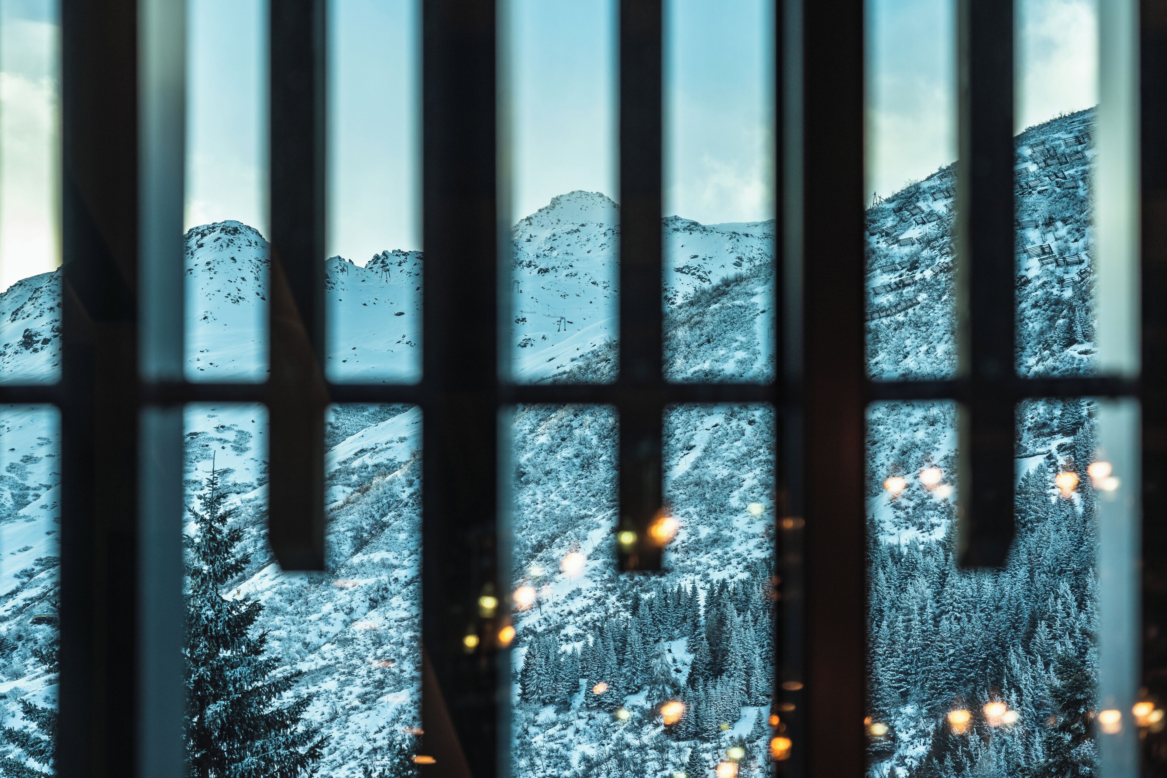 A view through bars of a mountainous landscape with snow-covered trees and a clear sky.