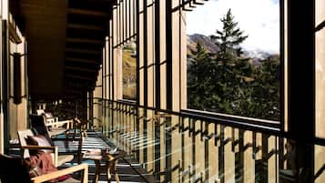 Een zonnig balkon met houten meubels en uitzicht op een bergachtig landschap.