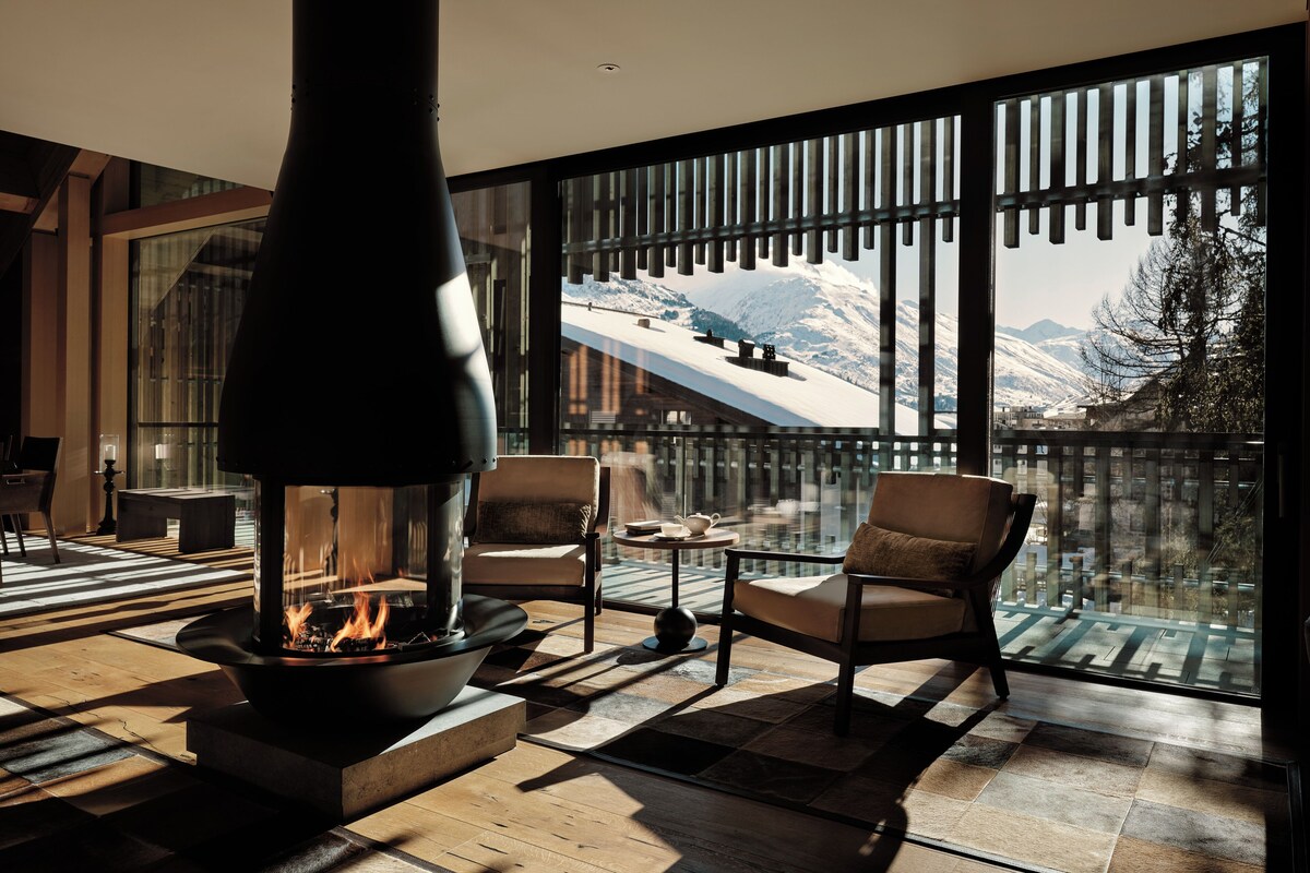 A modern interior with a wood-burning stove, comfortable seating, and a large window offering a mountain view.