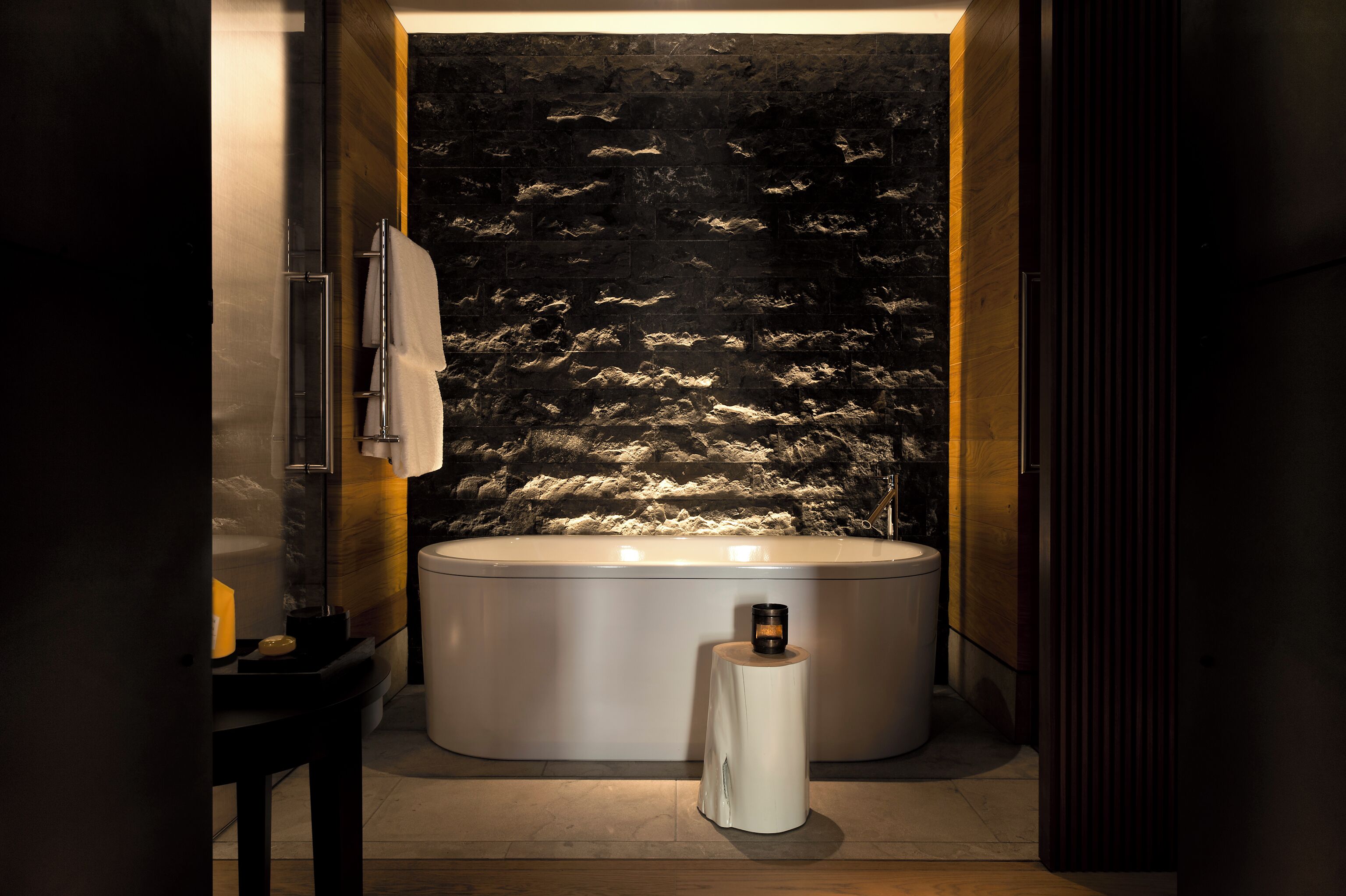 A modern bathroom with a freestanding bathtub, a towel rack, and a small table with a candle.
