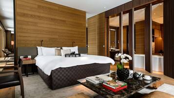 Una habitación de hotel moderna con una cama grande, una pared de madera, una zona de comedor con una mesa y sillas, y vistas al baño.