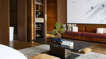 A modern living room with a wooden accent wall, a sofa, a coffee table with books, a bonsai tree, and a large screen displaying a ski scene.
