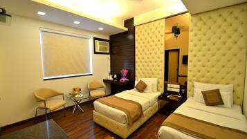 A hotel room with two beds, a small table, a chair, and a window with blinds.