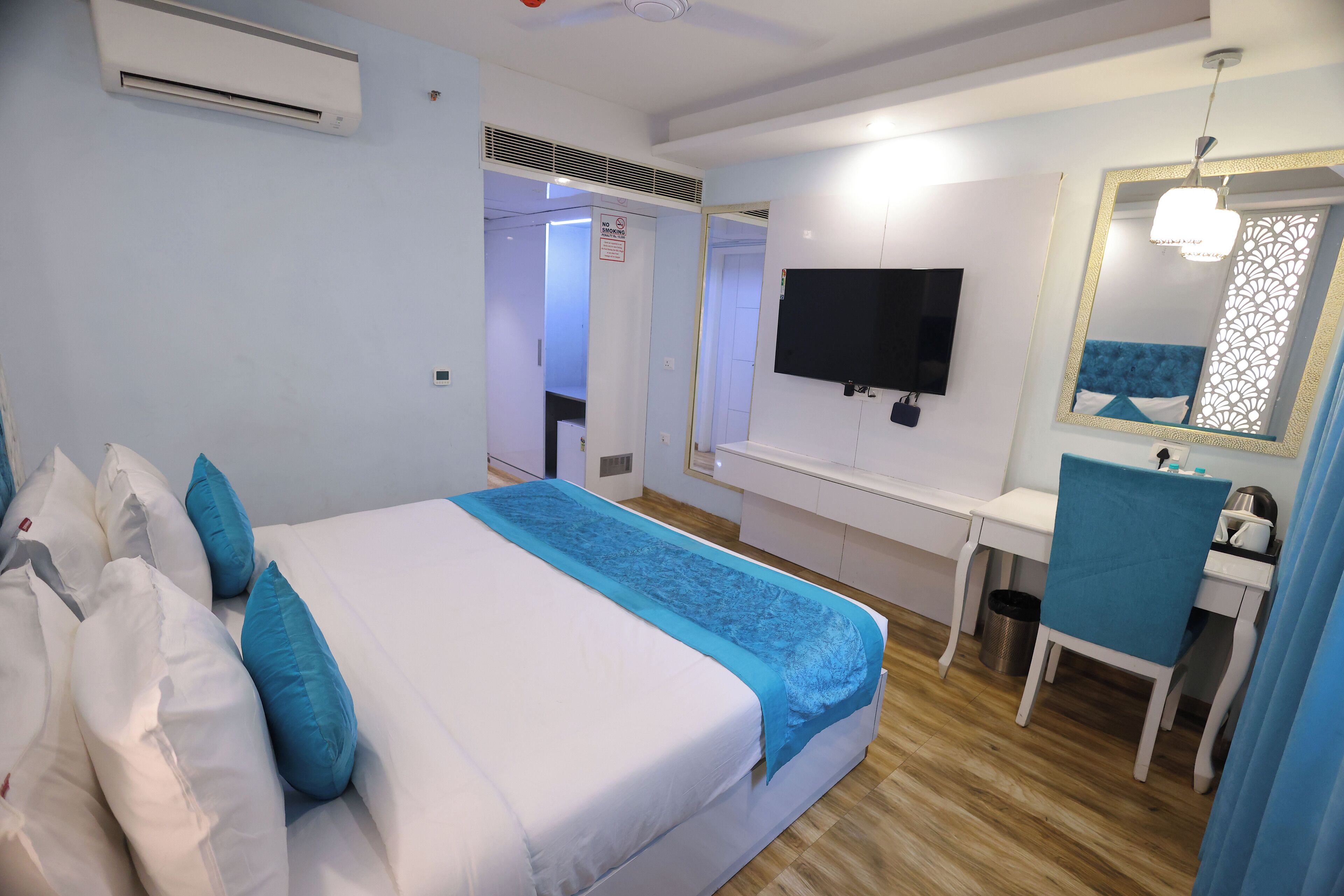 Habitación de hotel con cama, escritorio, silla, televisor y espejo.
