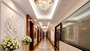 Un pasillo de hotel con piso de mármol, una araña y dos arreglos florales.
