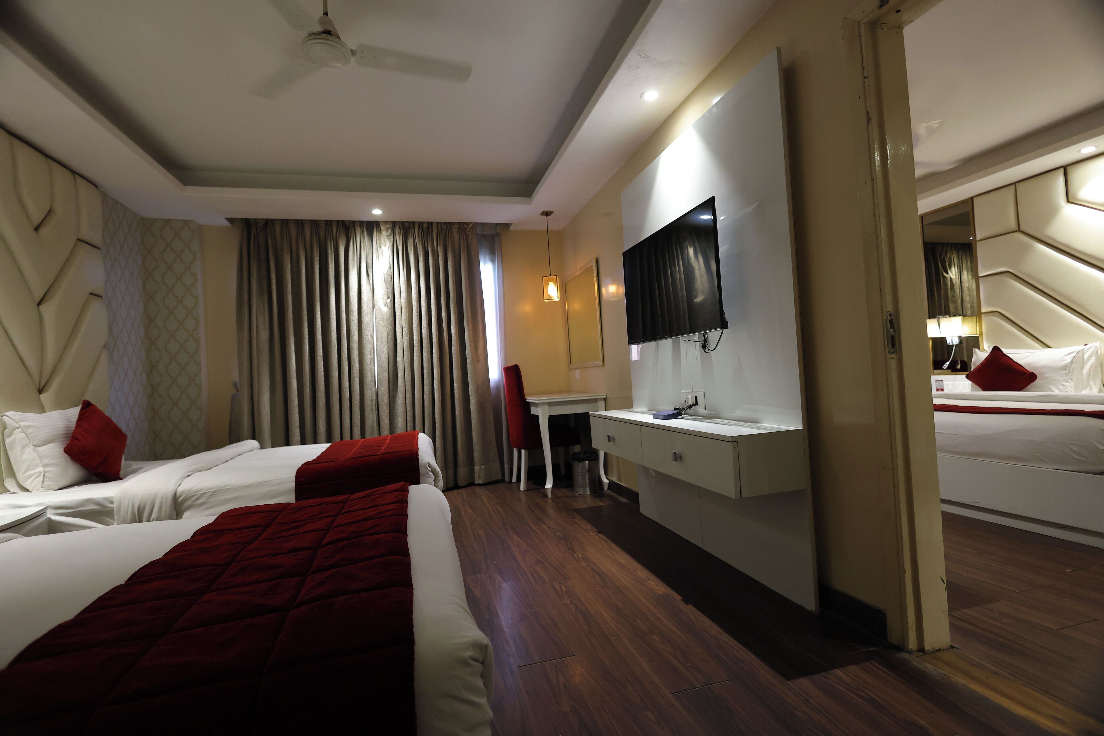 A hotel room with two beds, a desk, a TV, and a mirror.