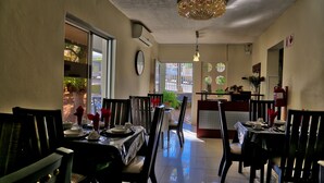 Uma sala de jantar com mesas para quatro pessoas, cadeiras, um lustre e vista para o exterior.
