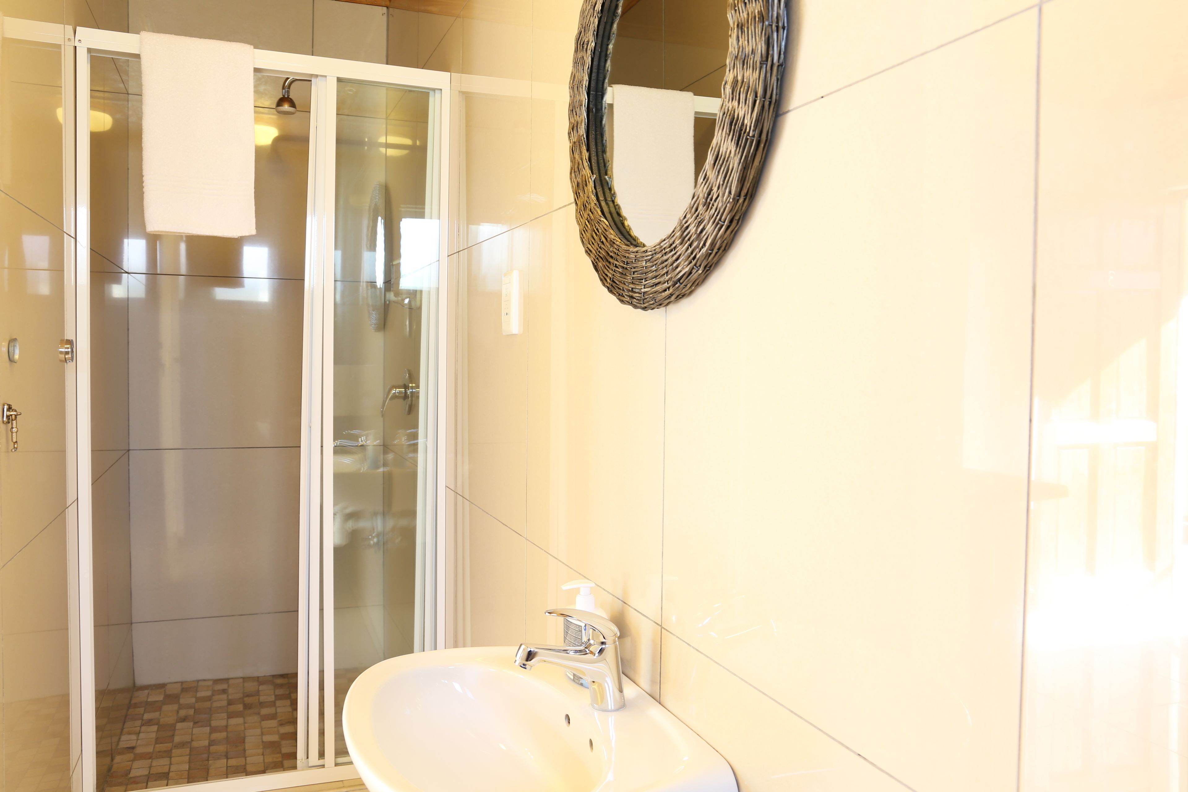 A bathroom with a glass shower enclosure, a white sink with a soap dispenser, and a woven wall decoration.