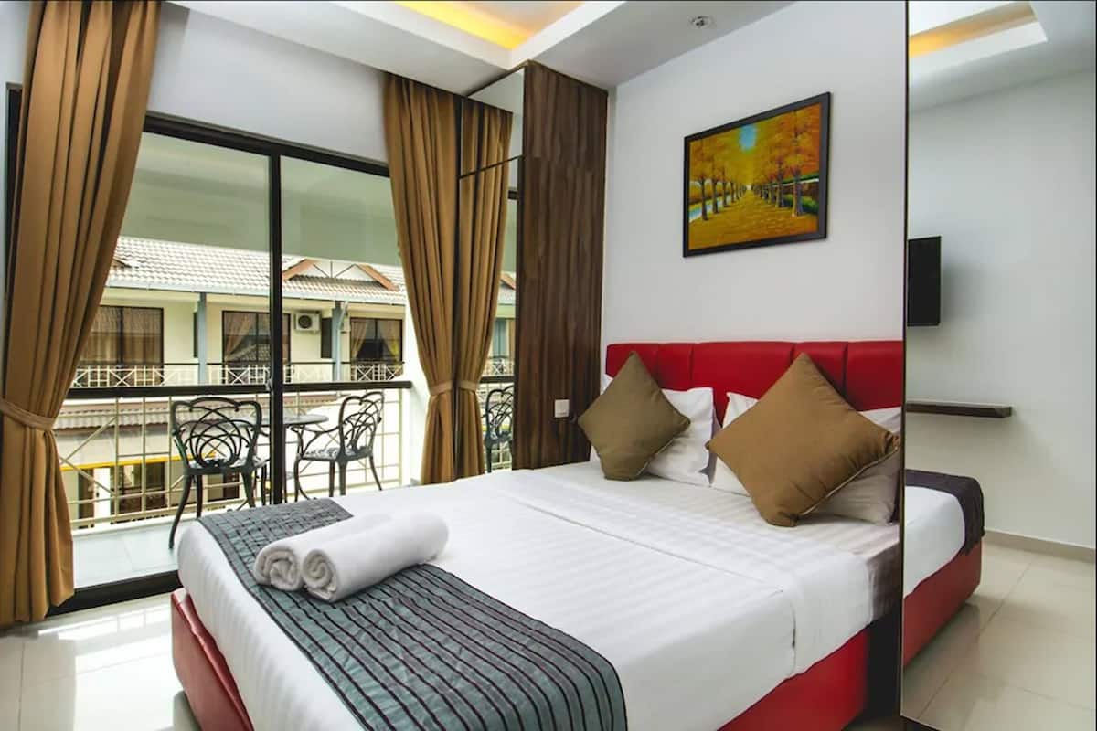 A hotel room with a large bed, red headboard, and a painting on the wall. There is a balcony with chairs and curtains.