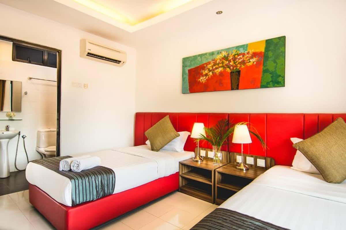 A hotel room with a red headboard, two beds, a painting on the wall, and a bathroom with a sink and toilet.