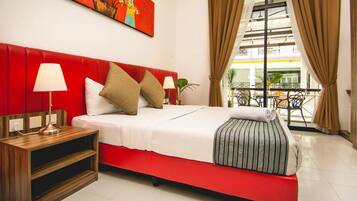 A hotel room with a red upholstered headboard, a white bedspread, and a view of the outside through large windows.