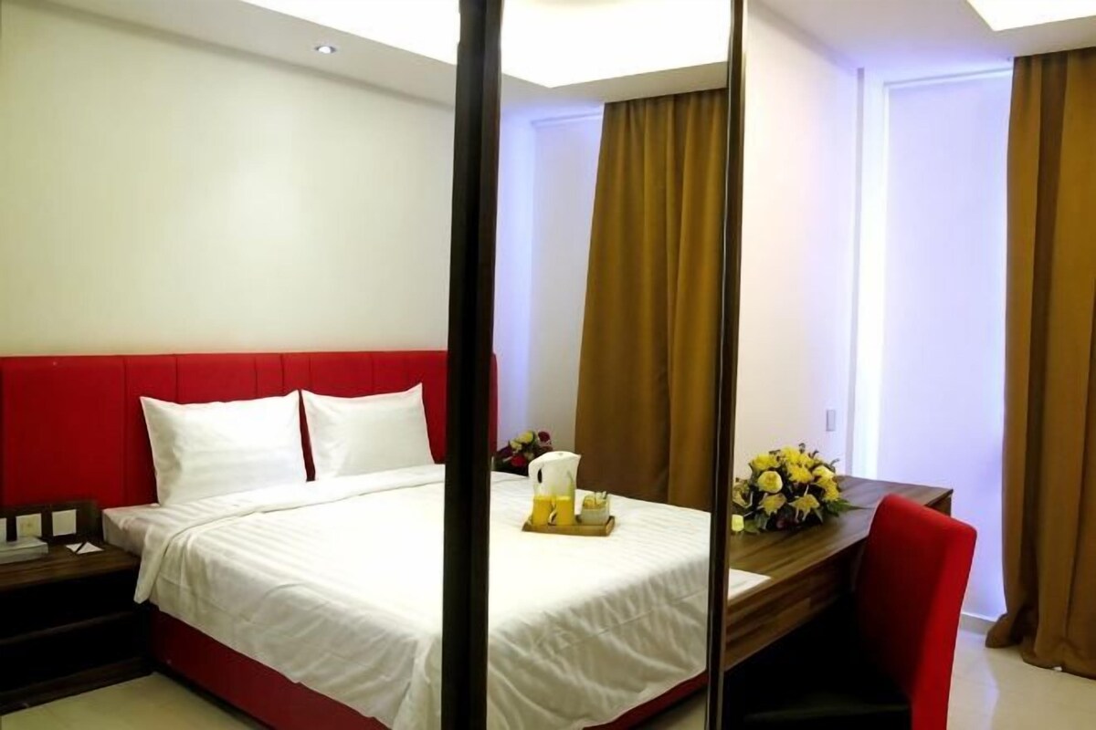 A hotel room with a bed, a desk, a chair, and a mirror.