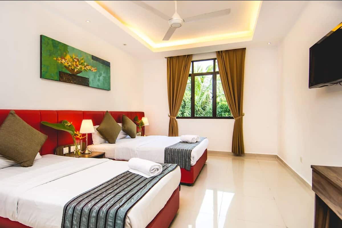 A hotel room with two beds, a ceiling fan, a TV, and a window with curtains.