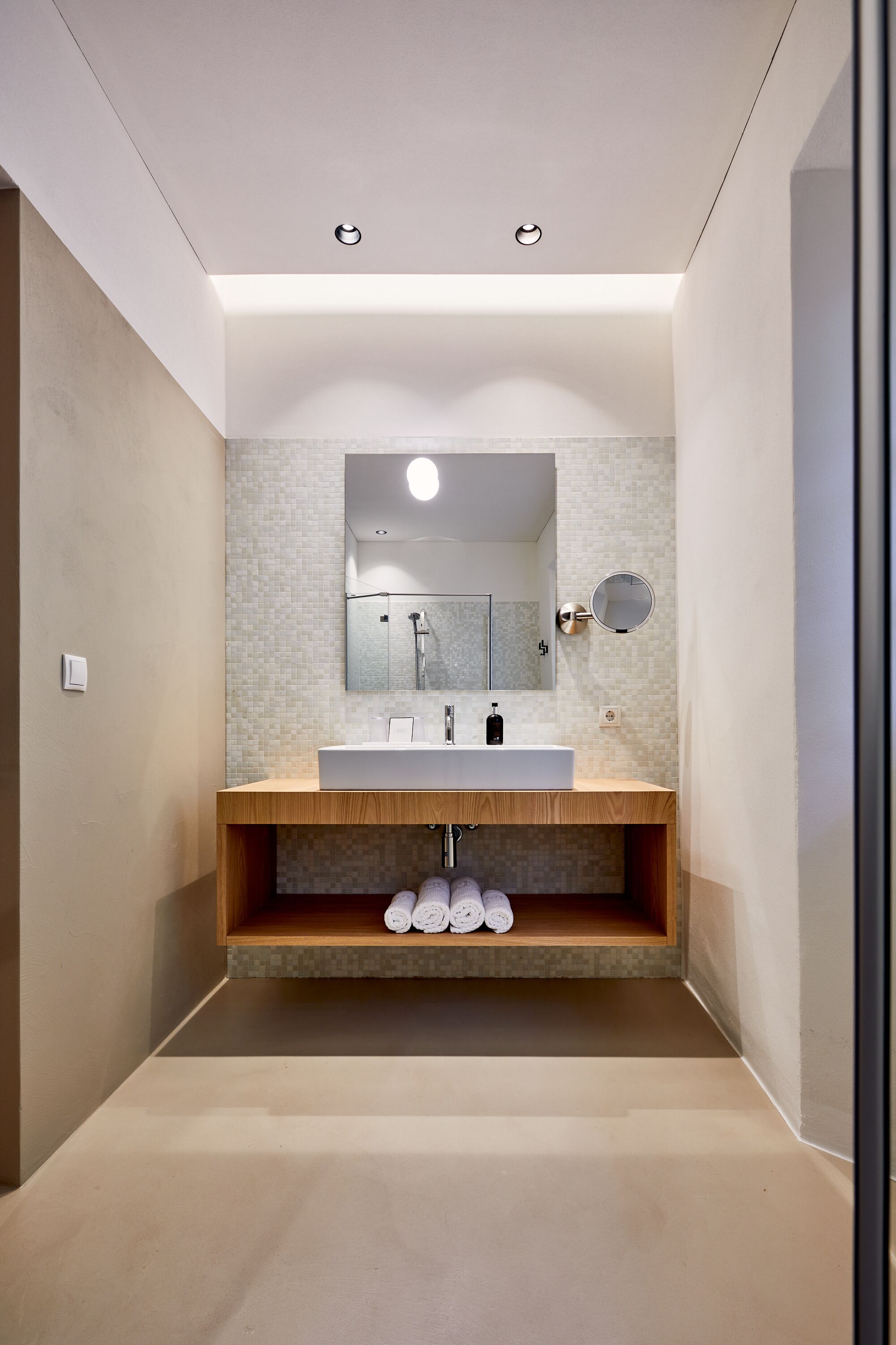 A modern bathroom with a wooden vanity, a large mirror, and a built-in shelf for towels.