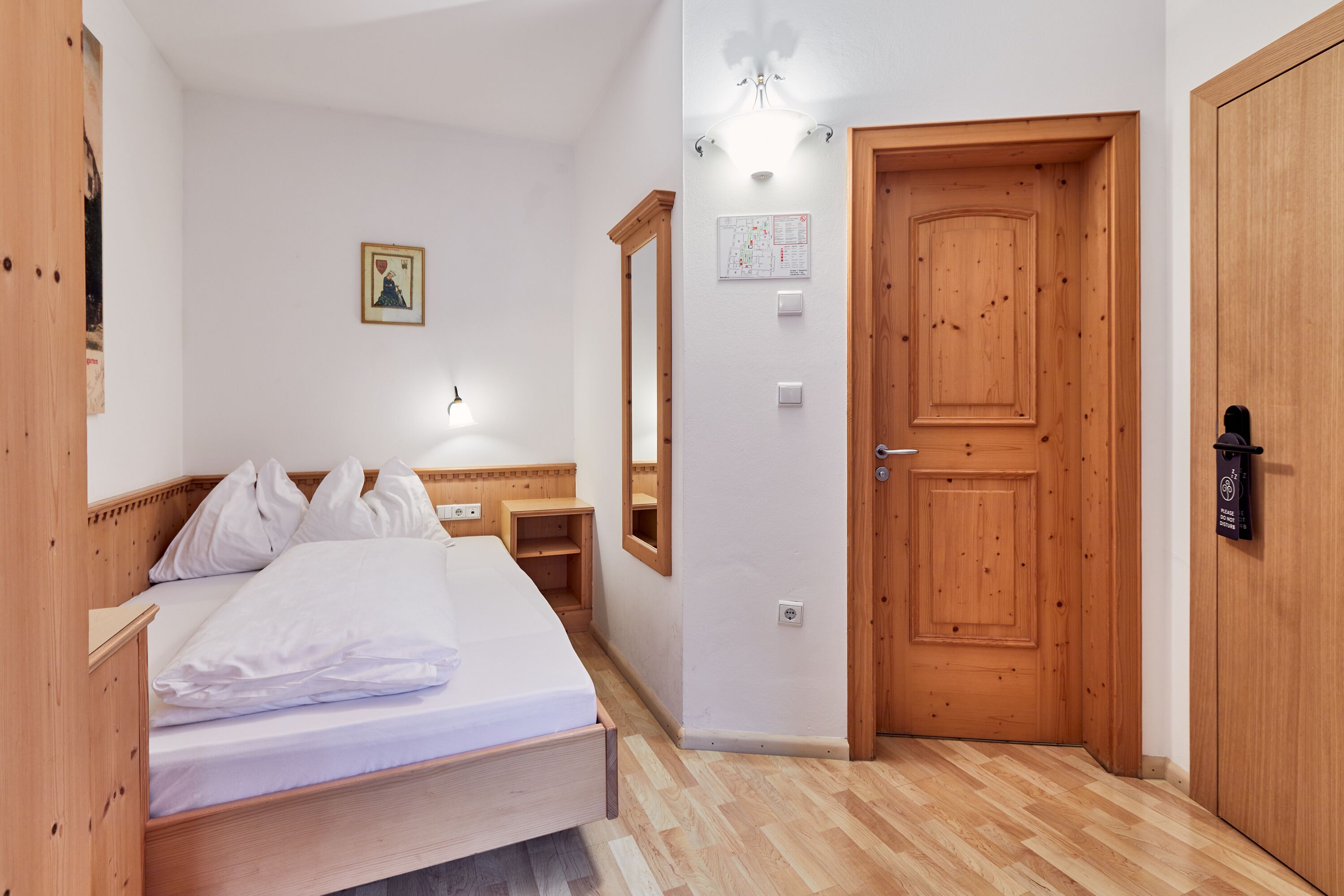 A bedroom with a wooden bed, a wooden wardrobe, a wooden door, and a wall-mounted light fixture.