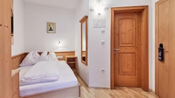 A bedroom with a wooden bed, a wooden wardrobe, a wooden door, and a wall-mounted light fixture.