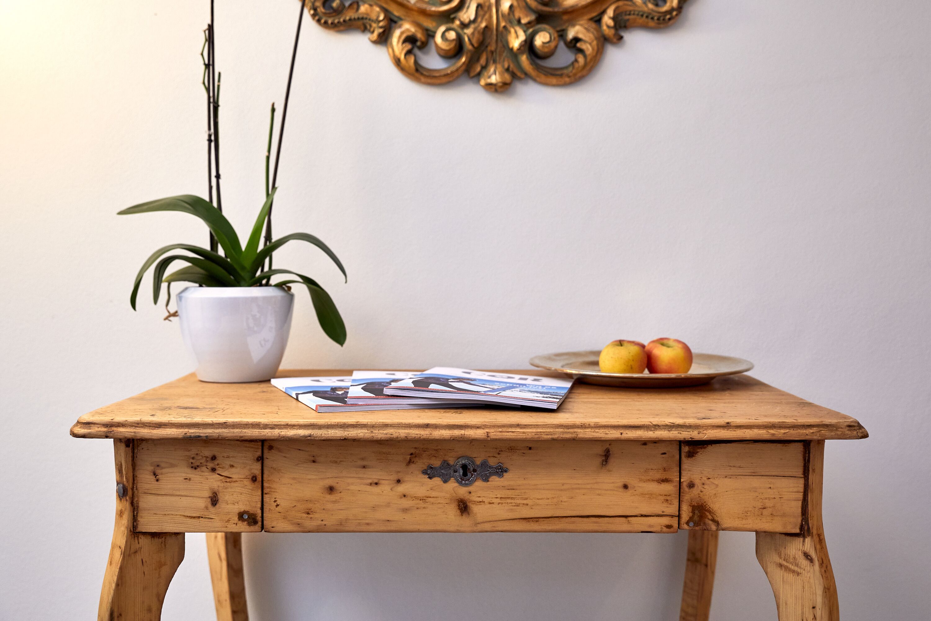 Una mesa de madera con un jarrón blanco, una planta en maceta y un plato de manzanas.