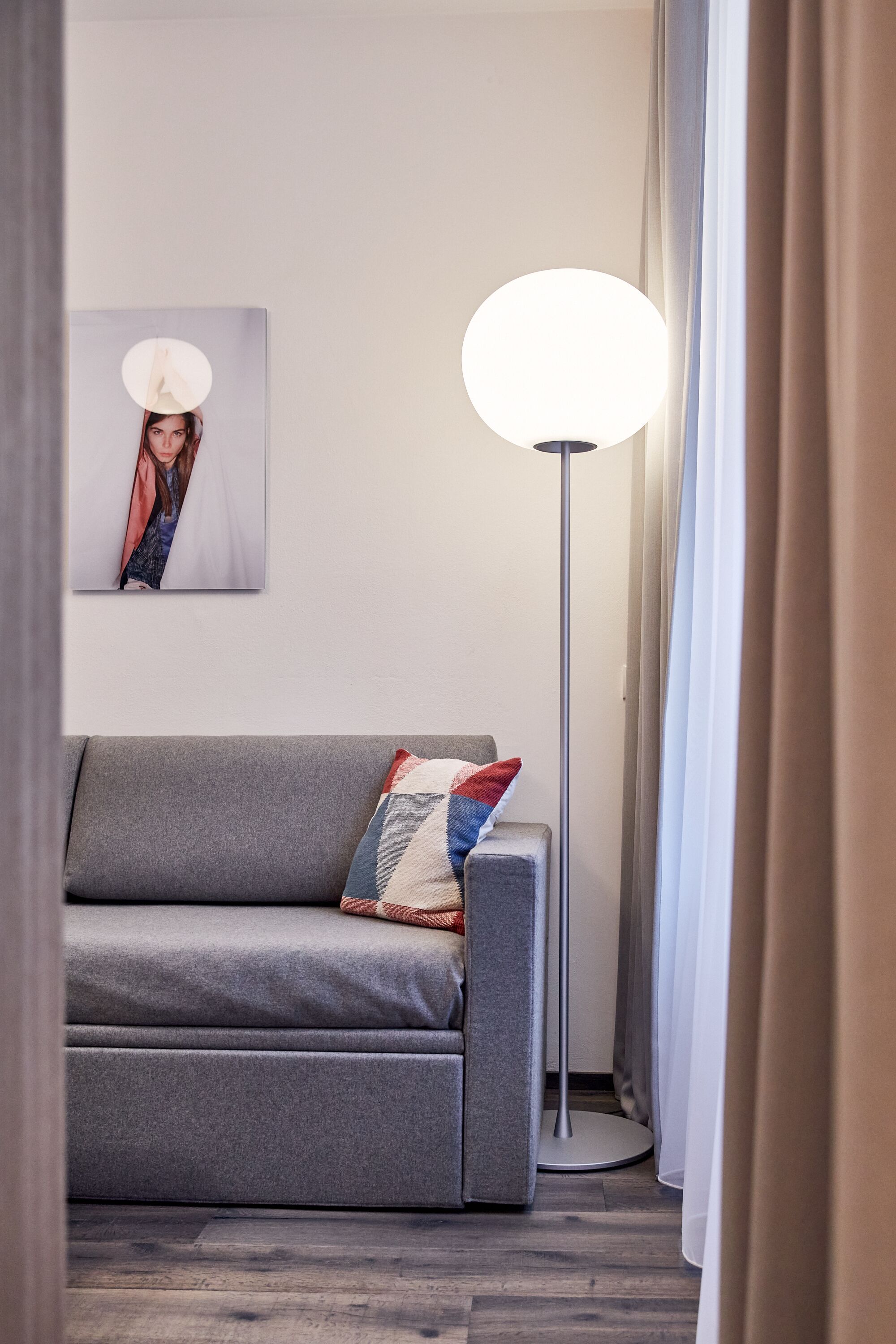 A modern living room with a grey sofa, a floor lamp, and a framed picture on the wall.