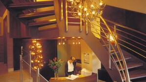 A modern interior with a wooden staircase, a reception desk, and a decorative light fixture. - Hotel Zaragoza Plaza (San Sebastián)