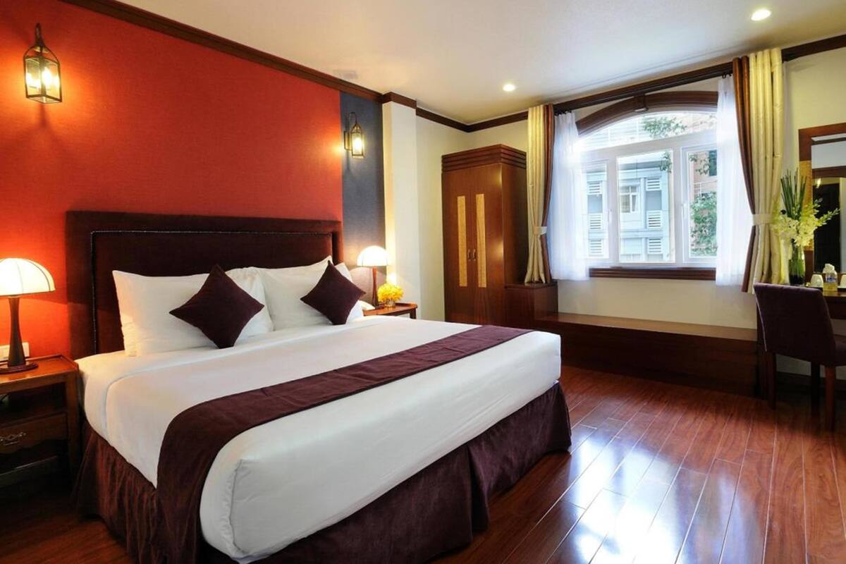 Ein Hotelzimmer mit einem großen Bett, Holzboden, einer roten Akzentwand, einem Holzschrank und einem Fenster mit Vorhängen.