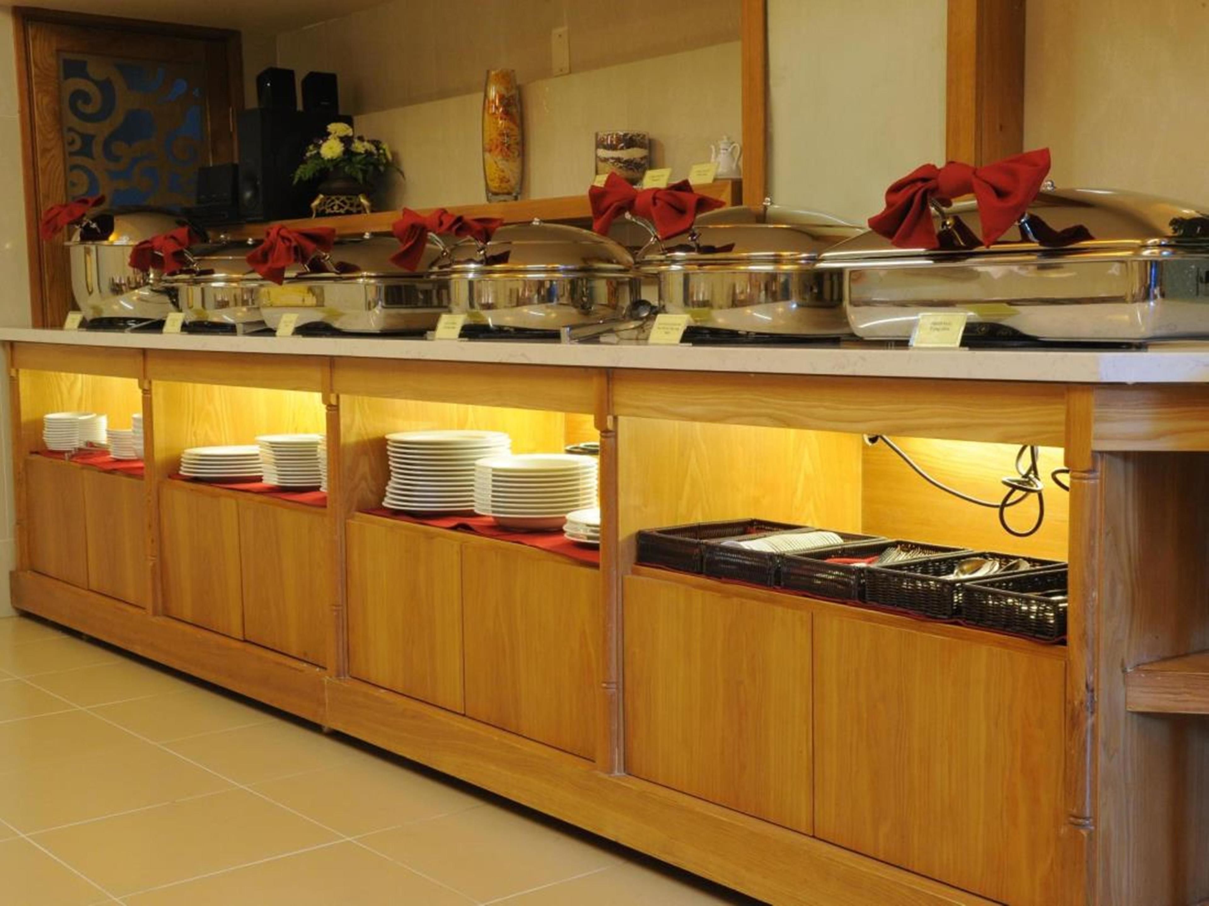 A buffet setup with multiple serving stations, each with a covered food container and a stack of white plates underneath.