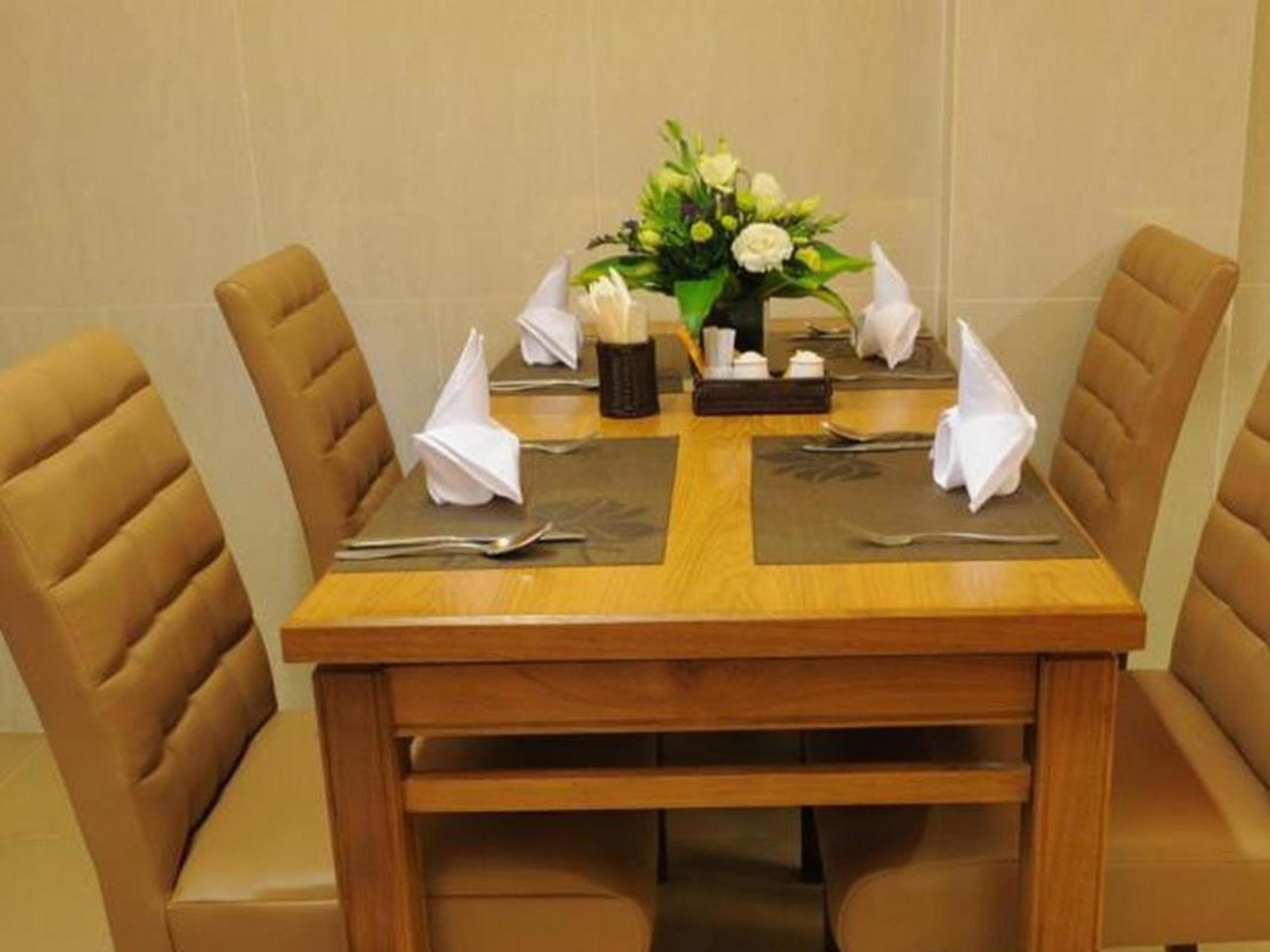 A dining table set with four chairs, a vase of flowers, and a small tray with condiments.