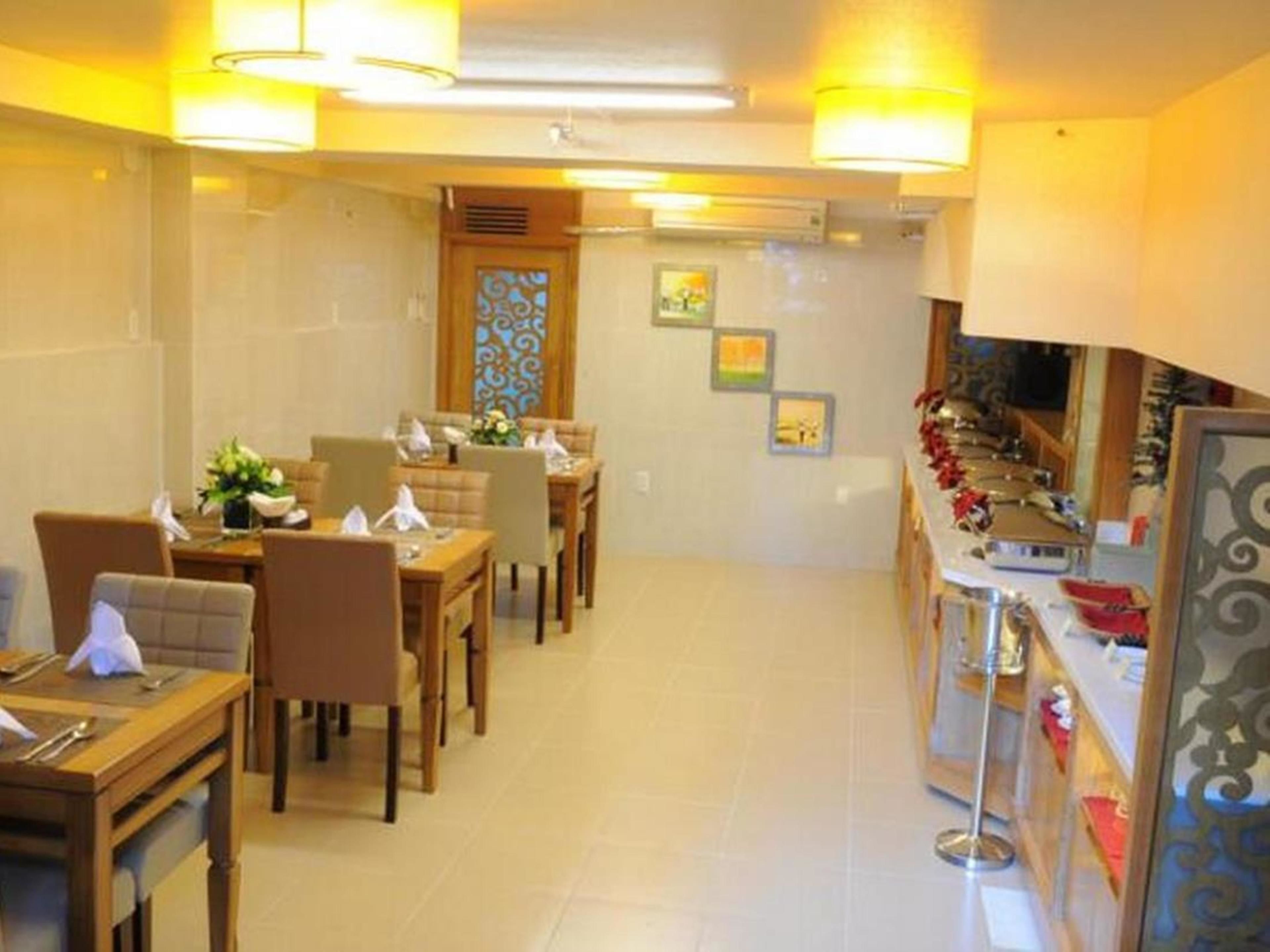 Un comedor con mesas y sillas de madera, una barra de buffet con separador de vidrio y obras de arte colgadas en la pared.