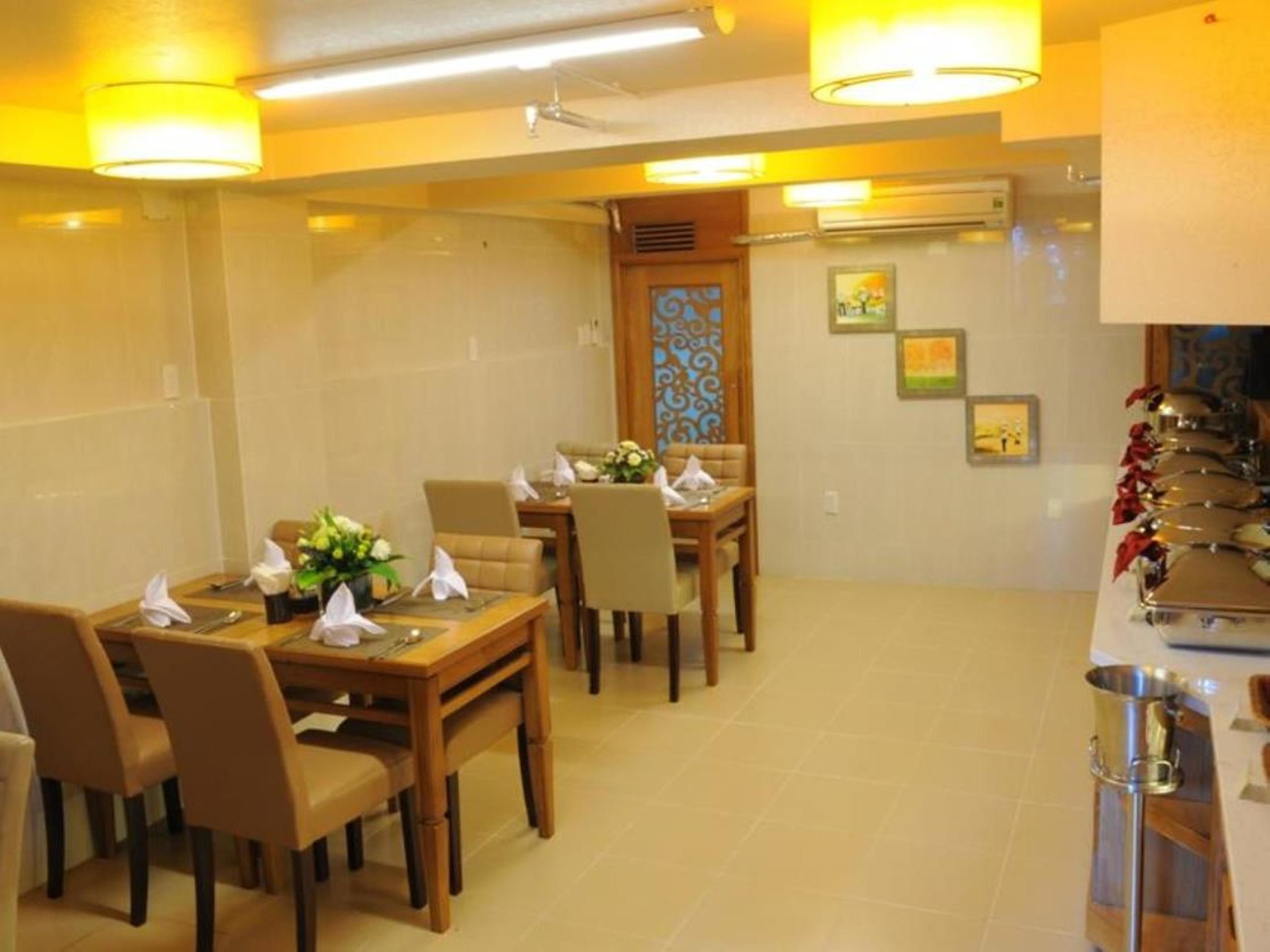 A dining area with a wooden table and chairs, a vase of flowers, and a kitchen area with a sink and utensils.