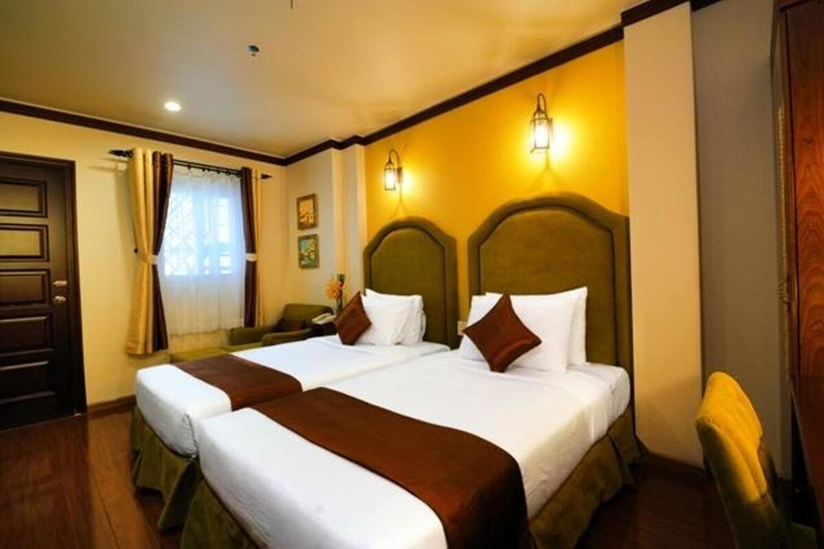 Ein Hotelzimmer mit zwei Betten, einer Holztür, einem mit Vorhängen versehenen Fenster und Wandleuchten.