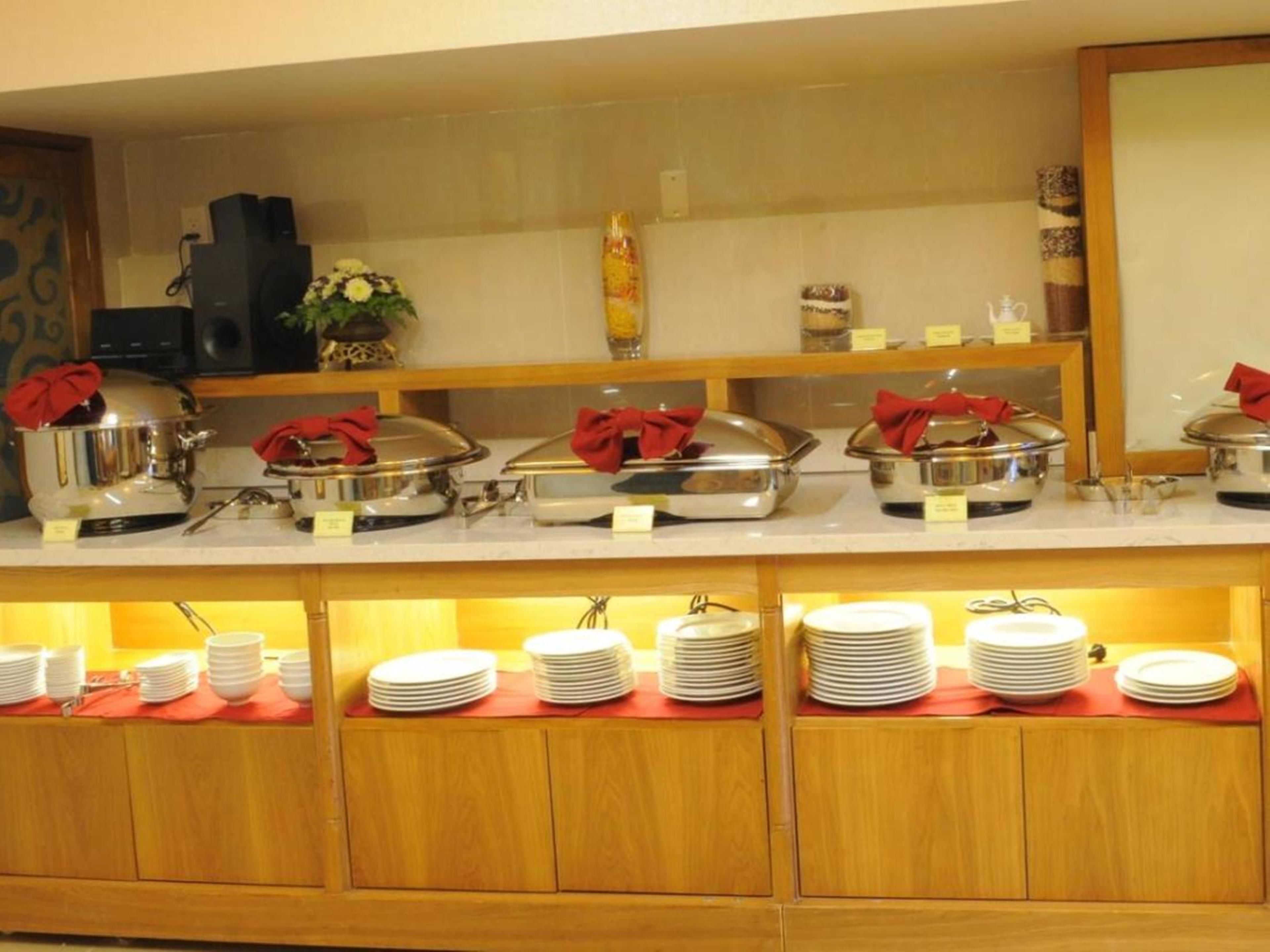 A buffet setup with covered food stations and stacked plates.