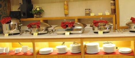 A buffet setup with covered food stations and stacked plates.