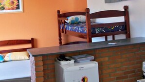 Una habitación con una cama litera, ventilador de techo, televisión montada en la pared y un separador de ladrillo.