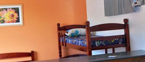 A room with a bunk bed, a ceiling fan, a television mounted on the wall, and a brick partition.
