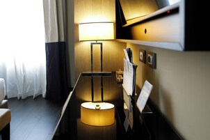 A hotel room with a bed, a bedside table, a lamp, a wall-mounted TV, and a window with curtains.