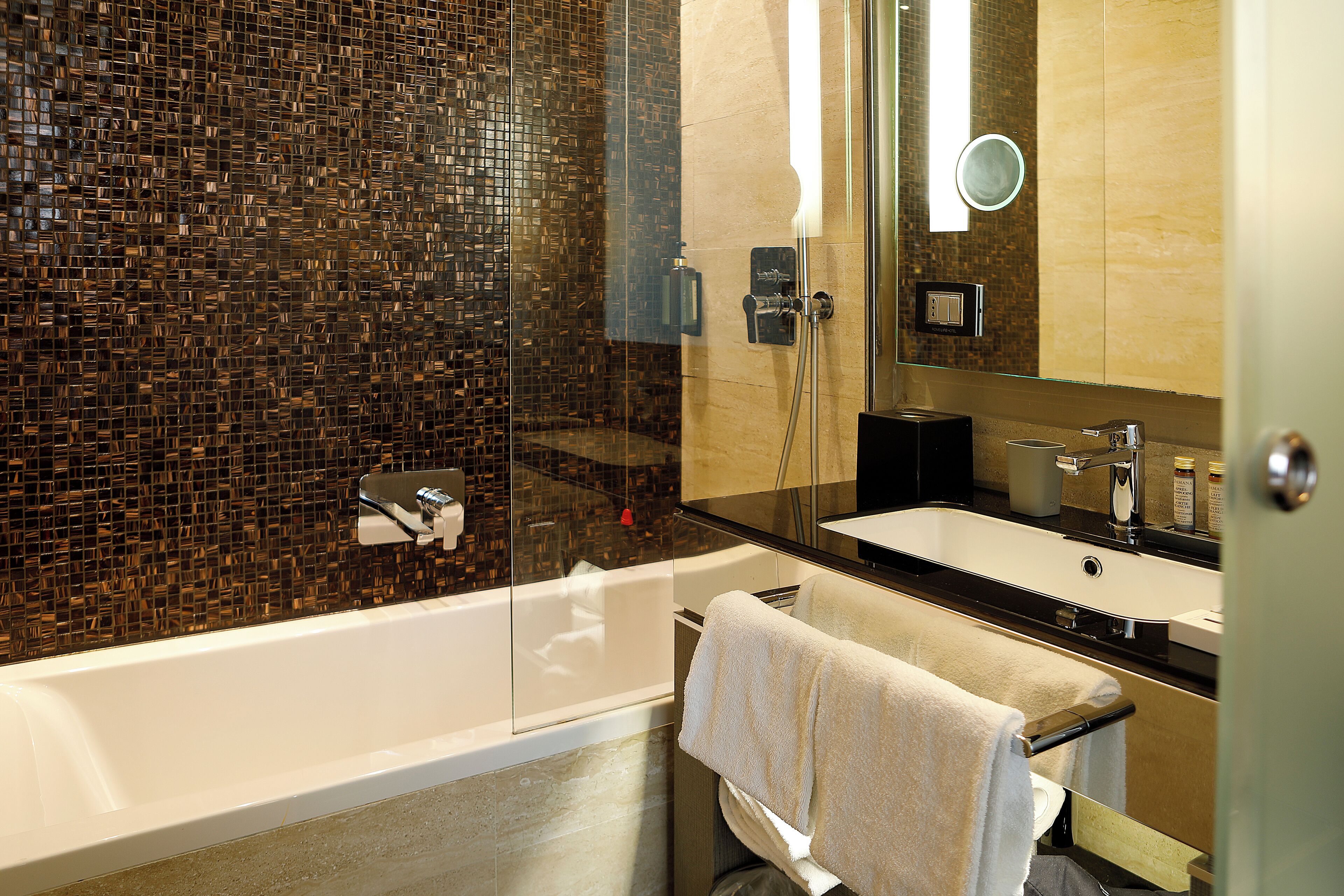A modern bathroom with a glass-enclosed shower, a white bathtub, and a black countertop sink.