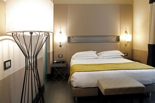 A hotel room with a bed, bedside table, lamp, and a floor lamp.