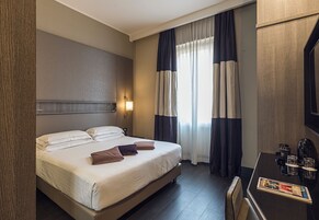 A hotel room with a bed, a desk with a magazine, and curtains.