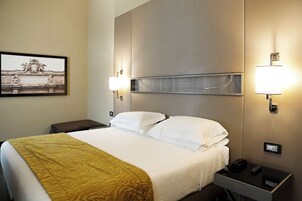 A hotel room with a large bed, two bedside lamps, a nightstand with a phone and a lamp, and a framed picture on the wall.