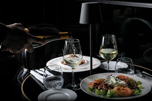 Una tavola imbandita con piatti di cibo, bicchieri d'acqua e vino, e una bottiglia che viene versata.