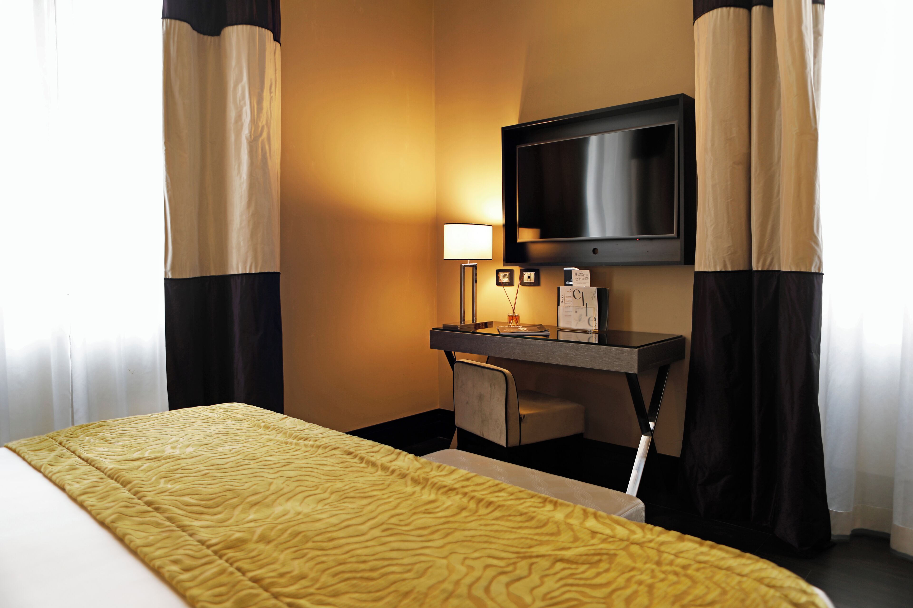 A hotel room with a bed, a desk, a television, and a lamp.