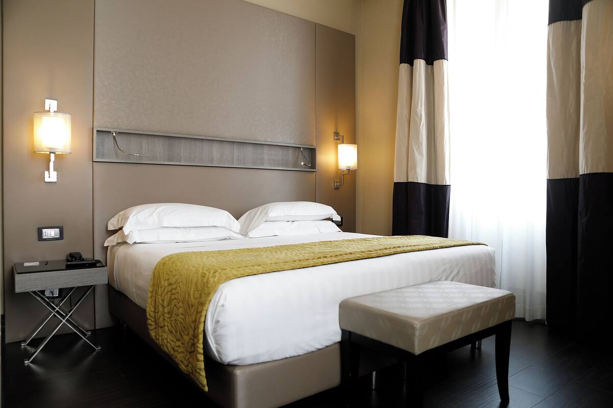 Ein Hotelzimmer mit Bett, Nachttisch, Lampe und Vorhängen.