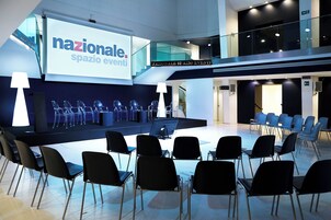 A conference room with a stage, chairs, and a large screen displaying "nazionale spazio eventi".
