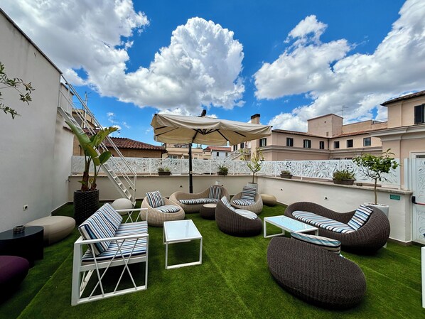 Un patio al aire libre con mobiliario de mimbre, una mesa blanca y un paraguas grande.
