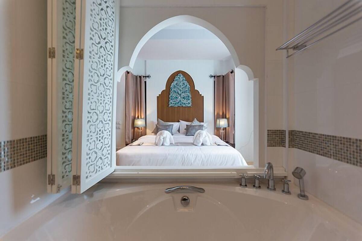 A hotel room with a large bed, a decorative headboard, a bathtub, and a shower area.