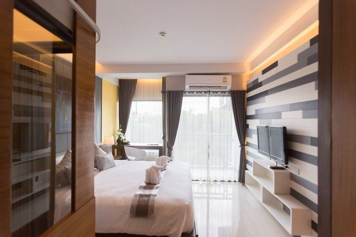 A modern hotel room with a large bed, a TV, and a window with curtains.