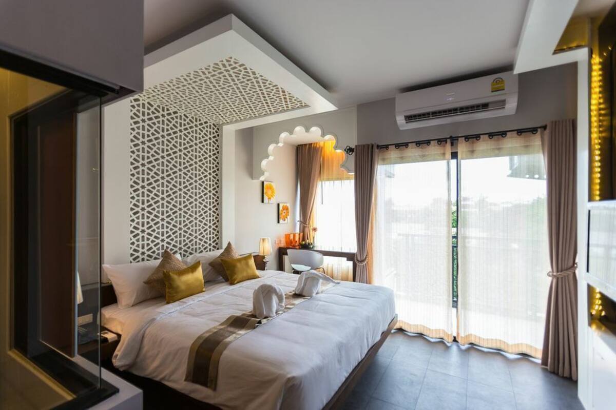 A hotel room with a large bed, a decorative wall, an air conditioning unit, and a view through the window.